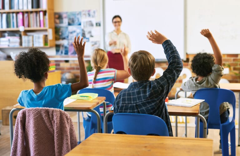 Una escena de clase con niños que levantan la mano para participar en la lección.