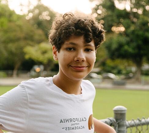Un estudiante que sonríe a la cámara y lleva una camiseta blanca con el logotipo de California Virtual Academies