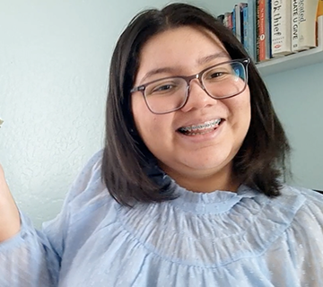 Una alumna de primaria que sonríe a la cámara. Tiene el pelo castaño, ortodoncia y gafas.